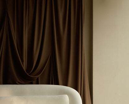 Brown curtain with a beige wall and white chair in the foreground